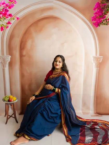 A full-length seated portrait in a traditional blue saree, with added floral elements to bring a touch of nature indoors.
