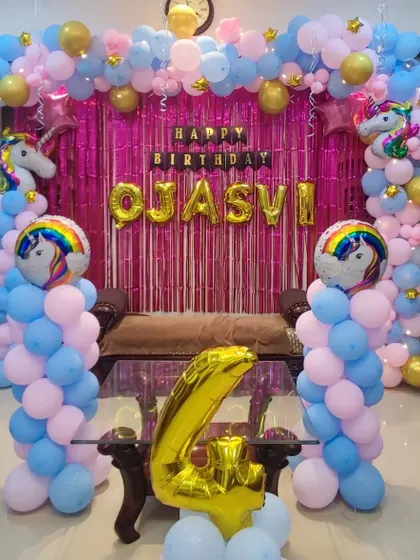 A unicorn-themed fourth birthday party using a pink, blue, and gold color palette. The decoration includes a full balloon arch over a couch, a shimmer backdrop, and several unicorn and rainbow foil balloons.