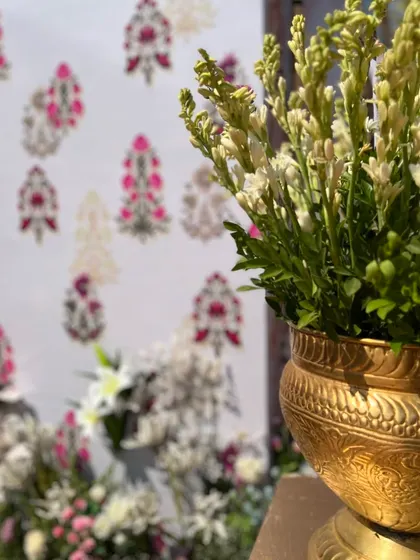 A close-up showing the contrast between the traditional floral motifs on the fabric panel and the fresh flowers in a brass pot.