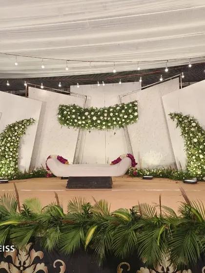 A contemporary stage design using angled white panels and asymmetrical floral arrangements. The clean lines and minimalist aesthetic are perfect for a modern wedding reception.