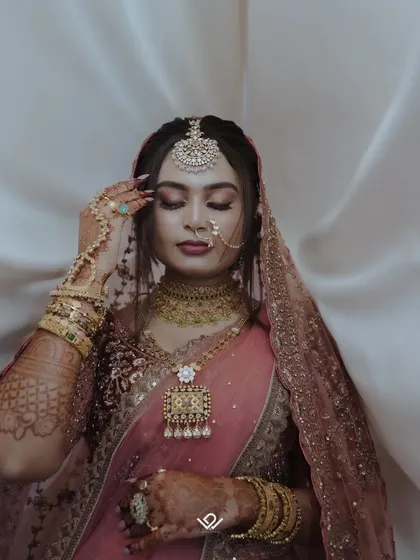 A close-up bridal portrait focusing on the stunning details of the maang tikka, nose ring, and intricate henna design.