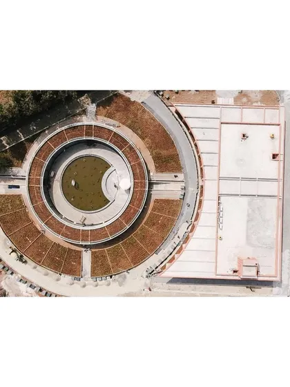 A top-down aerial view during the later stages of construction. This perspective clearly shows the concentric circles of the design, with the central water feature, the gallery walkway, and the outer green roof structure.