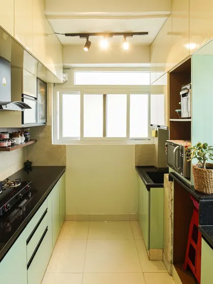 This parallel kitchen in a soft mint green is designed for maximum efficiency. The layout includes a tall unit with space for a microwave and open shelving, all within a compact footprint.