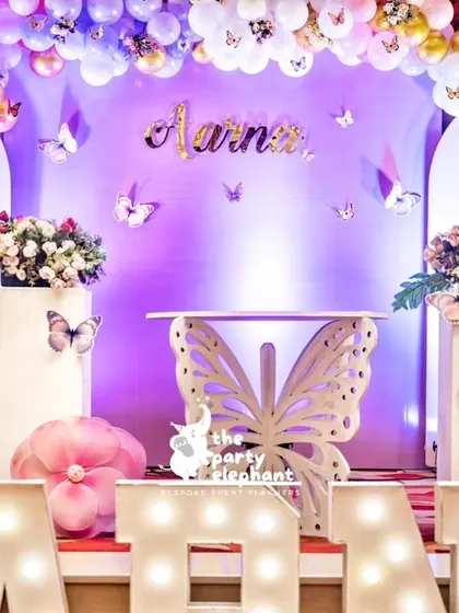 A closer look at the main stage, featuring a custom butterfly-shaped table for the cake. The decor is layered with fairy cutouts, floral arrangements, and whimsical mushroom props to build a rich, enchanted scene.