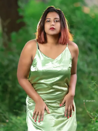 A confident and direct pose in a natural setting. The combination of the satin dress and the rustic background creates a striking contrast.
