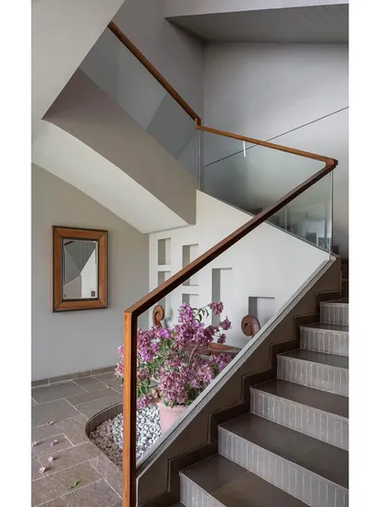 The staircase at Grove House is a sculptural element, with a glass balustrade and wooden handrail that maintain a sense of openness. An indoor planter at the base of the stairs brings a touch of nature inside, reinforcing the home's connection to its setting.