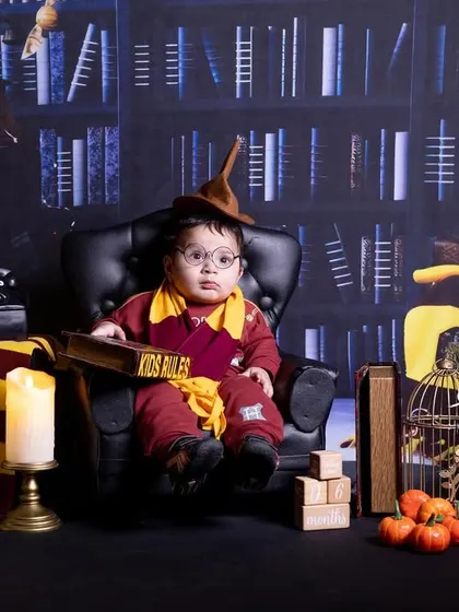 A baby dressed as a wizard, sitting in a large chair with a sorting hat, set against a magical library backdrop.