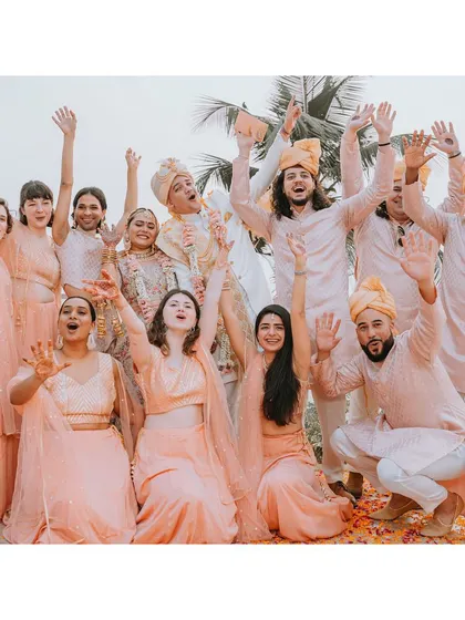 The whole wedding party joins in for a fun group photo. Dressed in coordinated pastel outfits, the bride, groom, and their friends and family celebrate together with joy and enthusiasm.