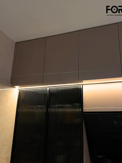 A detailed shot of fluted glass cabinet doors paired with handleless upper cabinets. The under-cabinet lighting highlights the texture of the glass and creates a warm, inviting glow on the countertop.