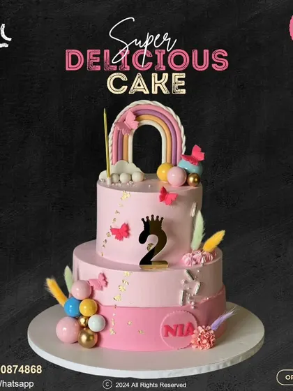 A stunning two-tier pink cake for a second birthday. This whimsical design is adorned with a rainbow, butterflies, feathers, and colorful spheres, creating a beautiful and festive look.