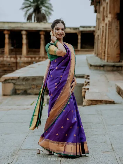 A beautiful solo portrait of the bride in her vibrant purple saree, standing gracefully within the ancient temple grounds.