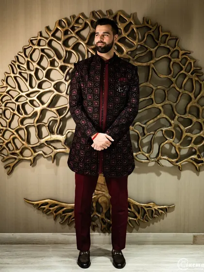 A full-length portrait of the groom looking sharp in his embroidered sherwani, posing against an artistic backdrop.
