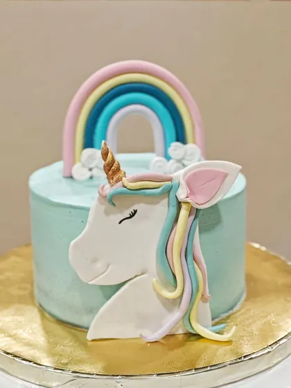 A full view of the unicorn theme cake. The simple, smooth buttercream finish makes the colorful fondant details really stand out.