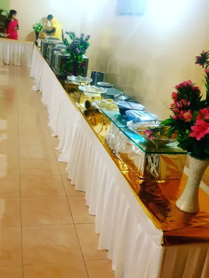 This image shows a long buffet table with a combination of glass-top risers and chafing dishes, decorated with simple flower arrangements.