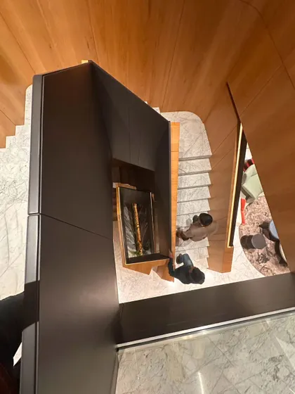 An overhead perspective of a staircase, highlighting the dynamic interplay of wood, grey matte paint, and marble. This view emphasizes the fluidity of the design, which guides movement while acting as a central art piece.