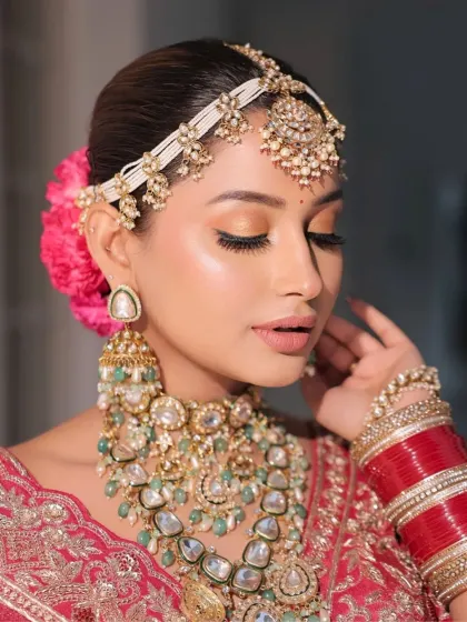 A close-up showcasing the soft, polished bridal glam. We focused on radiant skin and softly smoked eyes with a peach shimmer to complement her red lehenga and intricate jewelry.