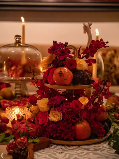 A tiered stand displays a beautiful arrangement of red and yellow roses, carnations, and pomegranates. This elevated centerpiece adds height and drama to the table design.
