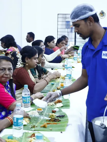 Our professional server, in full uniform with a hairnet and gloves, carefully serves rice to guests during a traditional banana leaf service, ensuring hygiene and attentiveness.