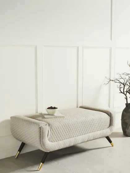 A minimalist upholstered bench with a unique quilted texture. The clean, white background and simple styling draw all attention to the product's form and detailed fabric.