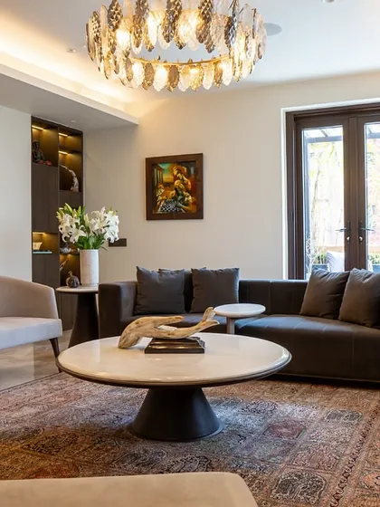 A cozy yet elegant living room arrangement. The dark sofa and armchairs are centered around a marble-topped coffee table, all under a striking chandelier. This space shows how we use bespoke furniture to create a sense of intimacy even in an open layout.
