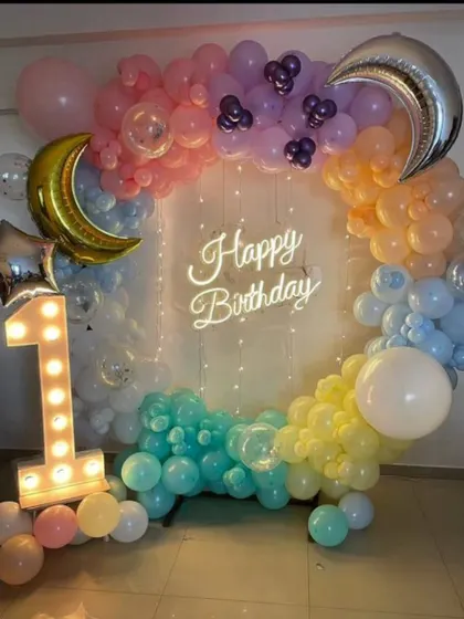 A dreamy "Twinkle Twinkle Little Star" first birthday theme. This setup features a rainbow pastel balloon circle, moon and star foil balloons, and a light-up number '1'.
