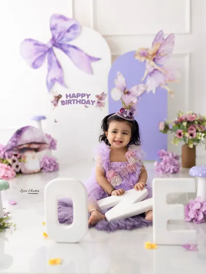 A magical fairy-themed first birthday. The birthday girl is dressed in a lovely purple dress, sitting with "ONE" letters in an enchanted forest setup.