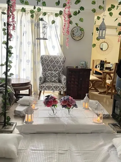 For a cozy and intimate gathering at home, I offer floor seating arrangements like this one. The setup includes comfortable mattresses and cushions, decorated with hanging vines, birdcages, and candle-lit lanterns to create a warm, inviting atmosphere.