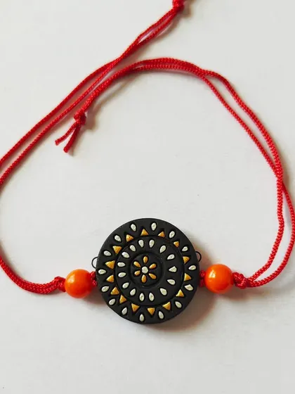 A black-based terracotta rakhi with intricate white and yellow dot work. These detailed pieces are perfect for making the festival of Rakshabandhan more vibrant.