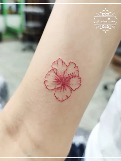 A single hibiscus flower outlined in red ink. This fine line floral tattoo is a great example of how a simple design with a single color can make a bold and beautiful statement.