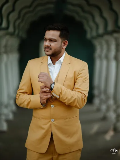 A dapper portrait of the groom in a stylish yellow suit, adjusting his cuffs in an elegant arched hallway.