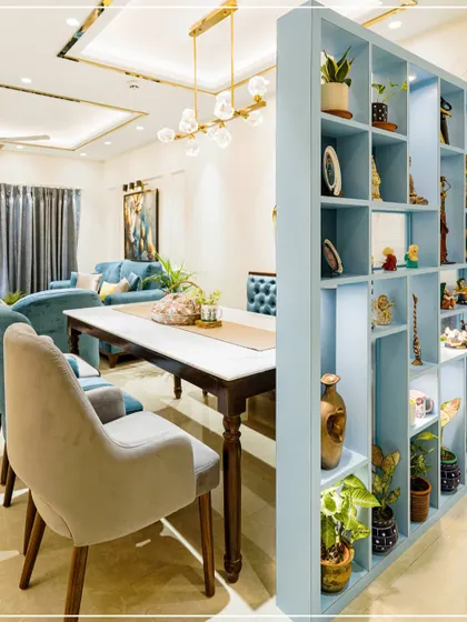 A dining area featuring a light blue shelving unit that acts as a partition, with a marble-top table and plush chairs.