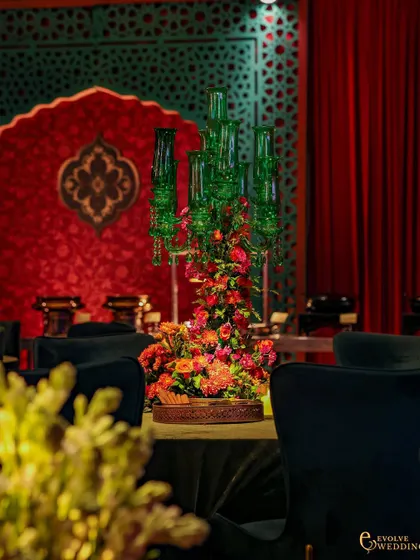 A green glass candelabra centerpiece, with the red and green decorative backdrops creating a cohesive color story. The focus on unique table decor elevates the guest experience.