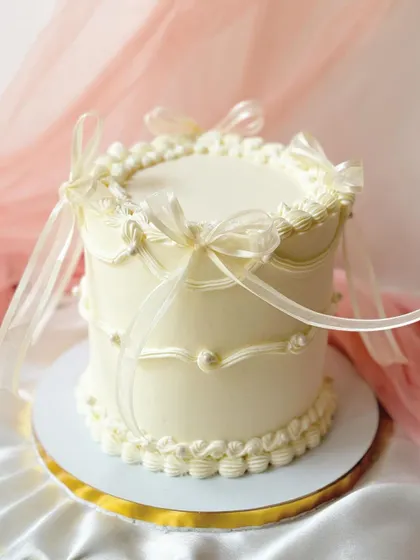 A pristine all-white cake with classic vintage piping and delicate ribbon bows. This timeless design is perfect for an elegant and understated celebration.