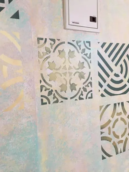 This angle highlights the subtle color variations in the underlying wall texture, which complements the darker stencil patterns. This custom wall was designed for a home's entryway.