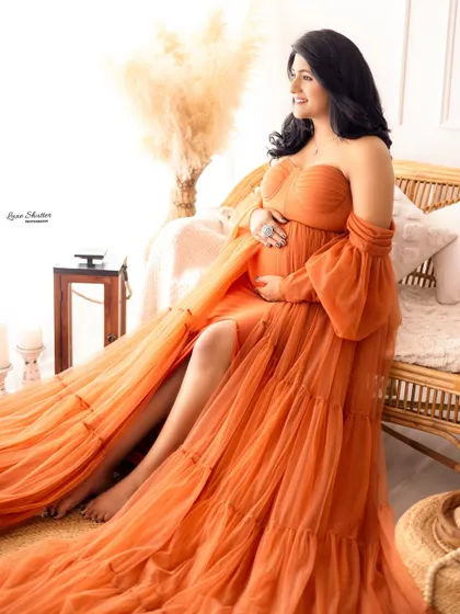 A relaxed and happy pose in a flowing orange gown, set in a cozy, boho-chic studio space.