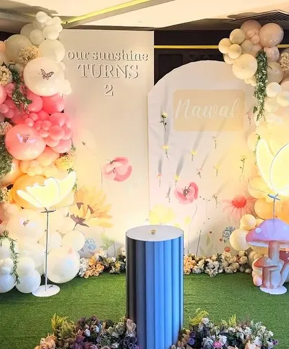 'Our Sunshine Turns 2'. This enchanting butterfly garden backdrop features two balloon arches, a custom name sign, and whimsical light-up mushroom and flower props.