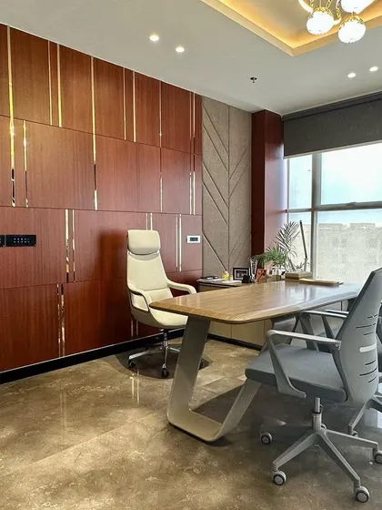 This executive cabin balances authority with modern design. The room features a custom wood-paneled wall with metallic inlays, a sleek executive desk, and large windows for ample natural light, creating a productive and sophisticated leadership space.