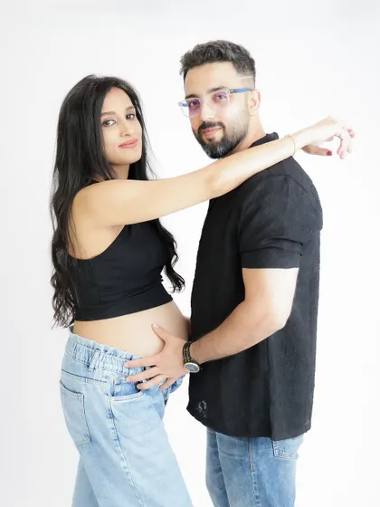 A modern and casual couple's portrait. The mom-to-be shows off her bump in a crop top and jeans, sharing a sweet moment with her partner.
