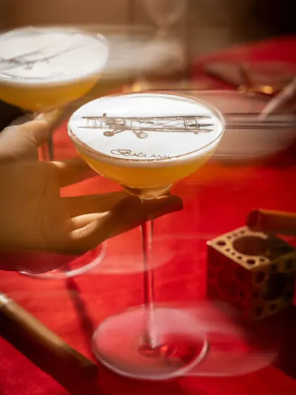 A conceptual cocktail at Baglami with an airplane stencil on the foam. The motion blur and smoky atmosphere evoke a sense of vintage travel and adventure, telling a story within the glass.