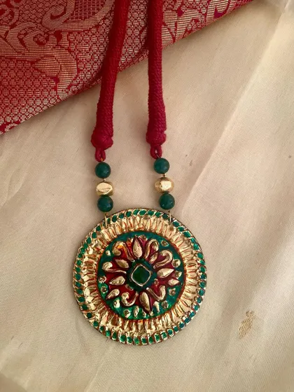 A different angle of the green and gold Tanjore-style pendant, highlighting the texture and color combination.