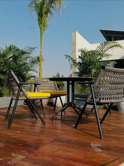 A cozy dining setup on the Faridabad terrace. The wooden deck is surrounded by a living wall of areca palms, creating a private, tropical-inspired corner for meals.