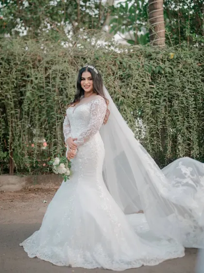 A full-length portrait of the bride in her gorgeous white gown and flowing veil, set against a natural green backdrop.