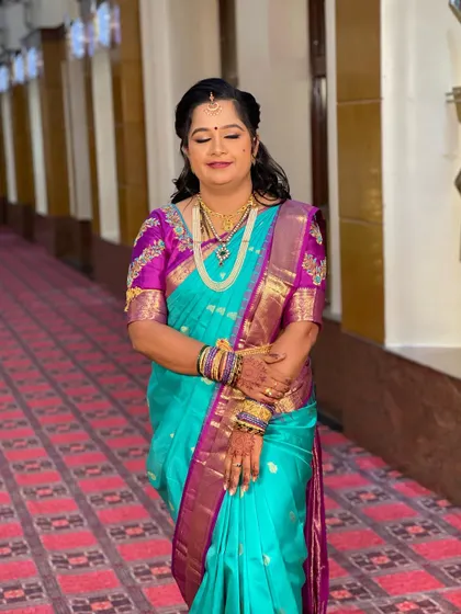 Swathi looking serene and beautiful for her reception. The turquoise and magenta saree is a vibrant choice, and her makeup is kept soft and elegant to complement it.