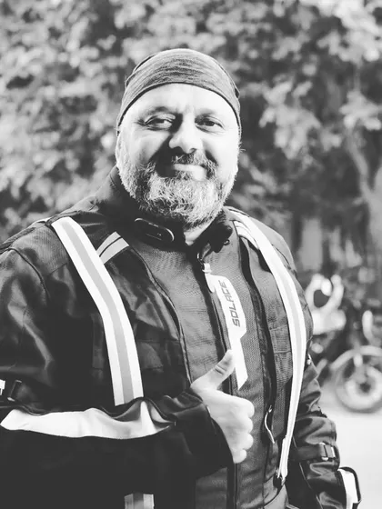 A warm, friendly portrait of a rider in a black and white finish. His smile and thumbs-up gesture perfectly capture the welcoming nature of the Royal Enfield tribe.