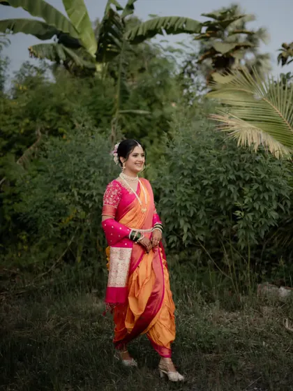 A full-length shot of the bride in her traditional nauvari saree, looking graceful in a natural, outdoor setting.
