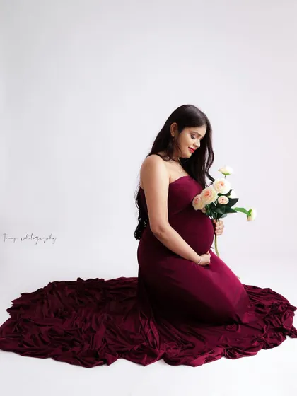 A sweet and simple portrait. The mom-to-be kneels in a rich burgundy gown, holding a small bouquet of white roses.