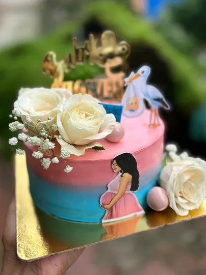 A beautiful baby shower cake with a pink and blue ombre design, topped with fresh white roses and a sweet illustration of a mom to be.