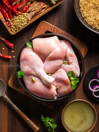 Raw chicken cuts, including drumsticks and breast pieces, arranged in a bowl with spices for making biryani.