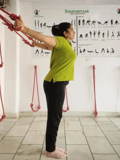 A side view of a student using the wall ropes. This method allows for a deep, supported stretch that helps decompress the spine and improve shoulder mobility, making it accessible even for those with stiffness.