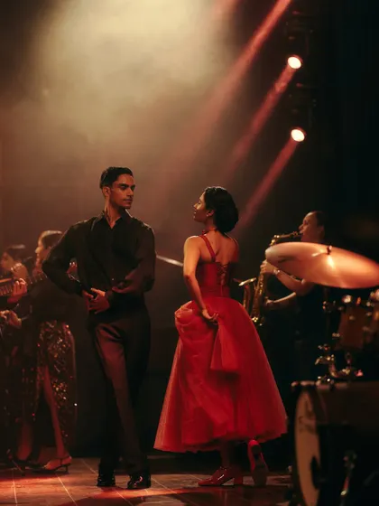 A candid moment between the lead dancers for the Origin & Ode campaign. The styling, with the vibrant red dress and classic menswear, was chosen to evoke a timeless, romantic feel.